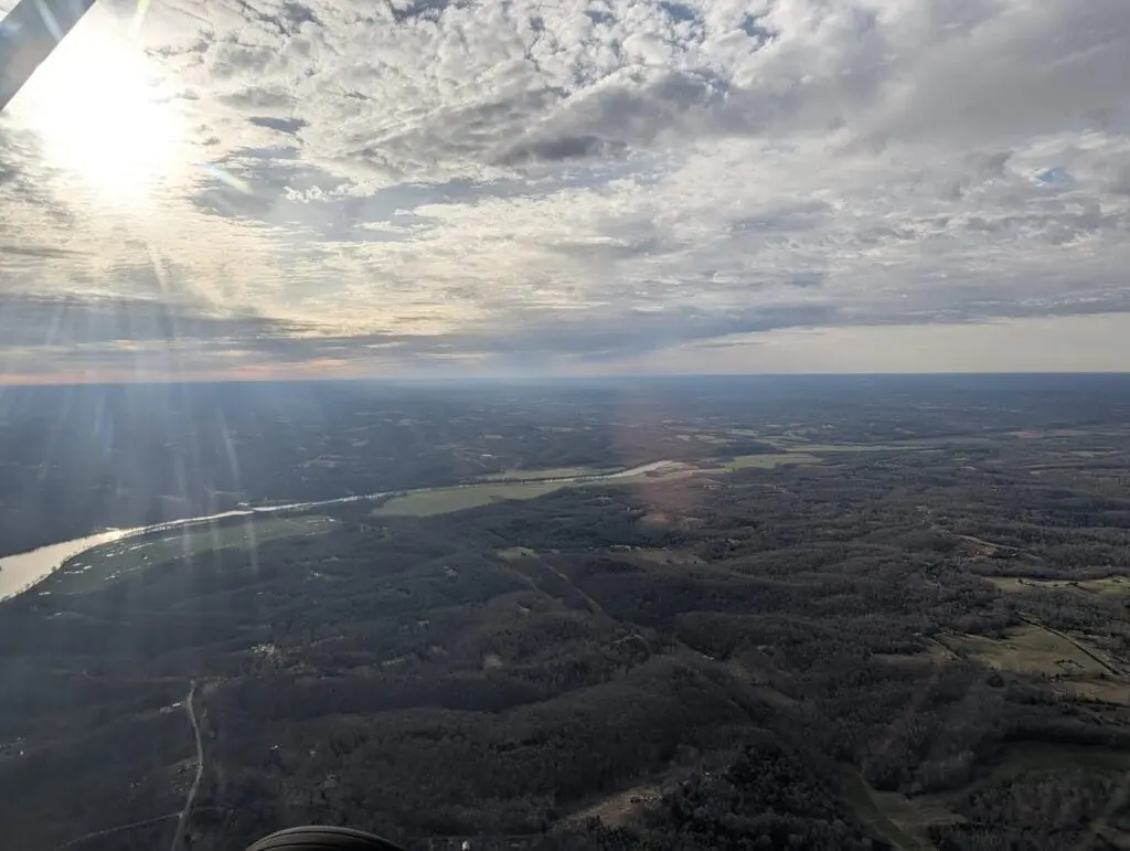 Aerial view of a river and wooded landscape beneath a cloud-filled sky