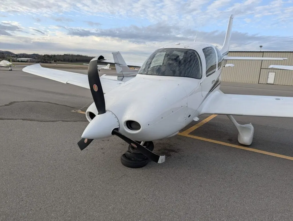 White Cessna parked on the tarmac with its nose supported and propeller close to the ground